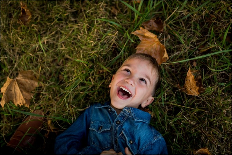 little boy in lying in the grass amongst the leaves