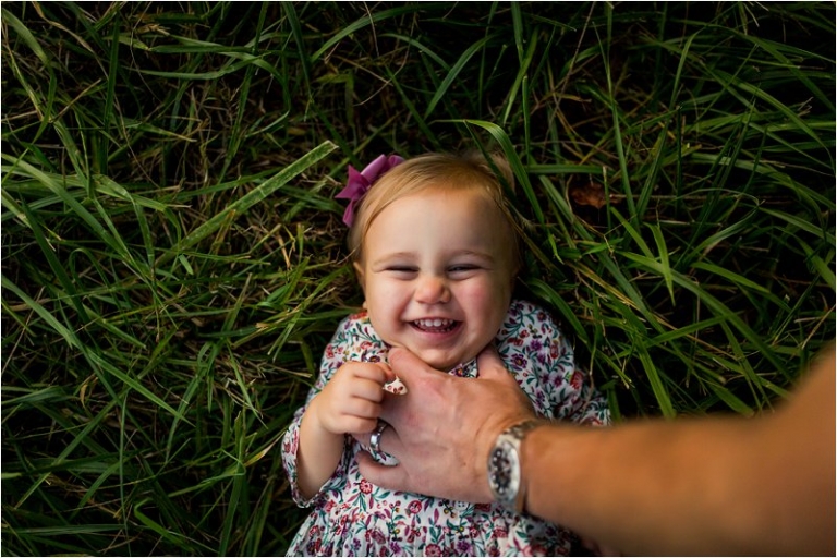 little girl lying in the grass with daddy tickling her