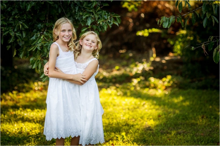 Sisters in white hugging in an outdoor setting
