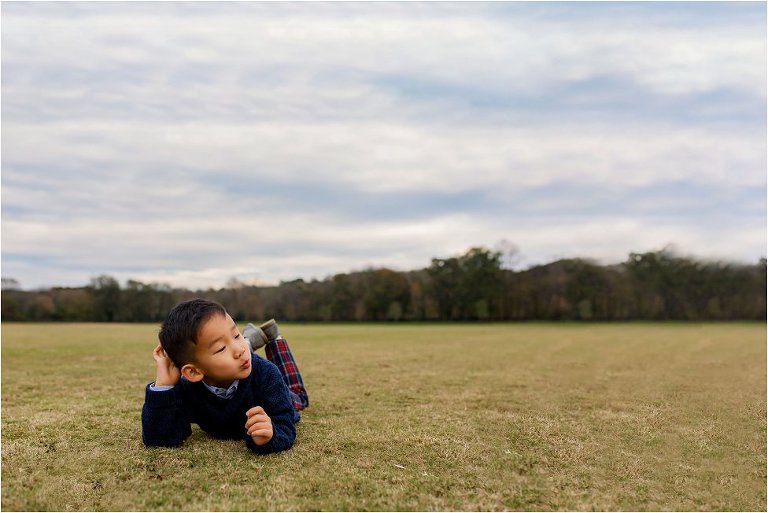 Sweet little boy in thinking man pose while laying on the ground. 