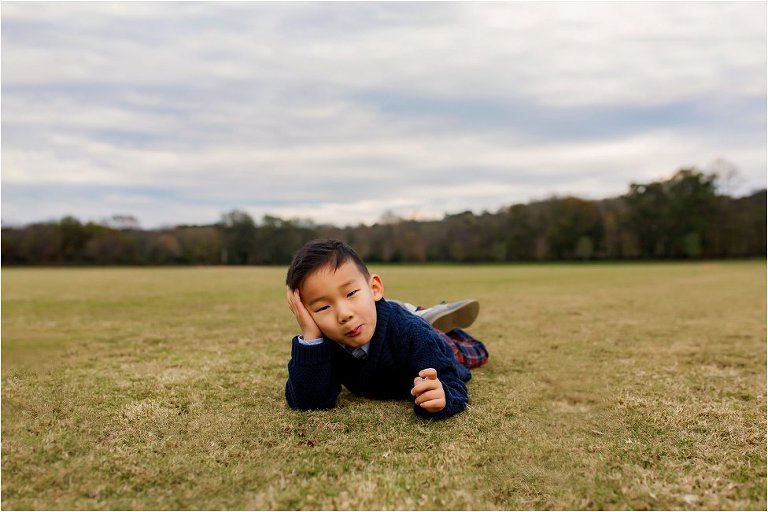 Little boy laying on the polo field in Vinings, head in hand, staring at the camera.