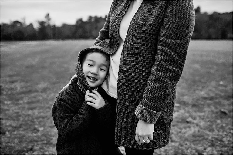 Little boy pulling his mom's blazer over his head.