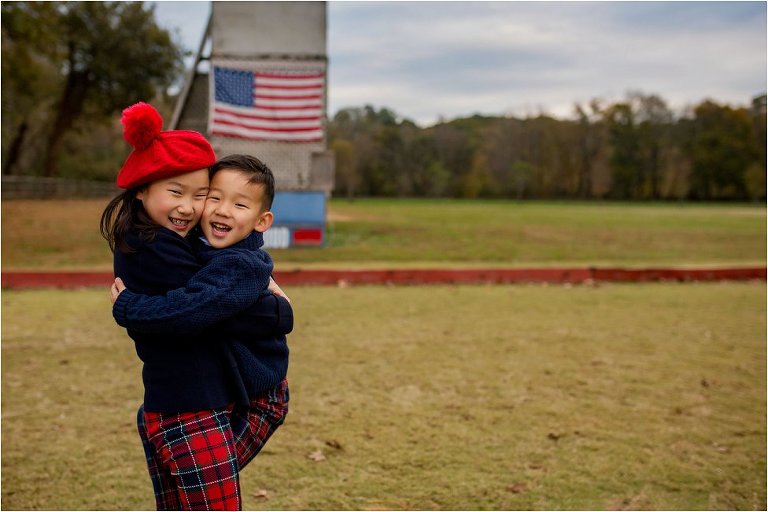 Little brother jumping in big sis's arms. Standing in front of American Flag.