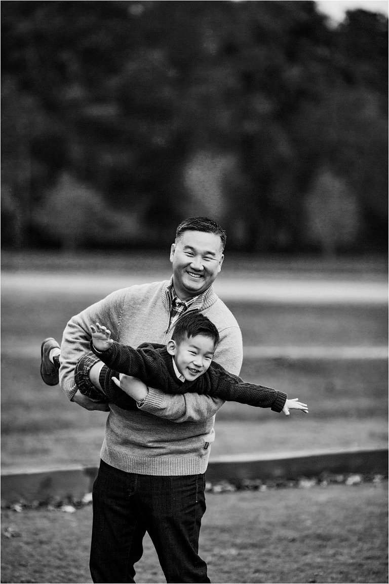 little boy playing airplane while his dad flies him through the air