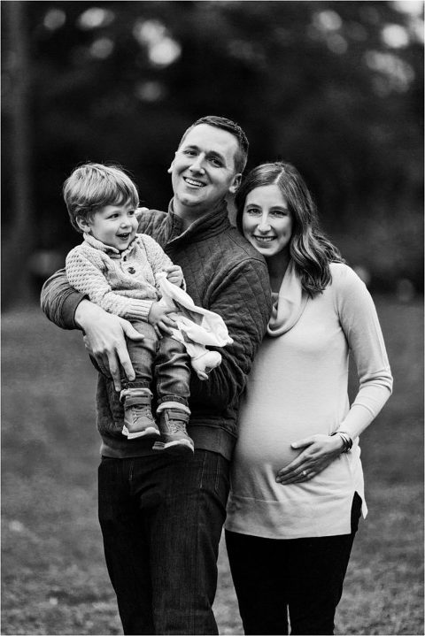 Mom to be with hand on belly, dad holding little boy 