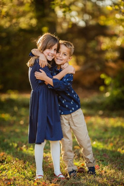 Sister and brother, both wearing blue, hugging each other.