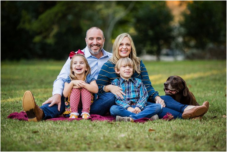 family of four posing for pictures with their beloved chocolate lab.