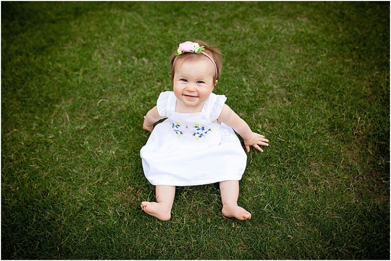 9 month old baby wearing white dress sitting in her backyard in Marietta, Georgia.