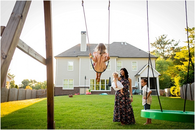 Little girl swinging high while her mom, baby sister, and big brother look on.