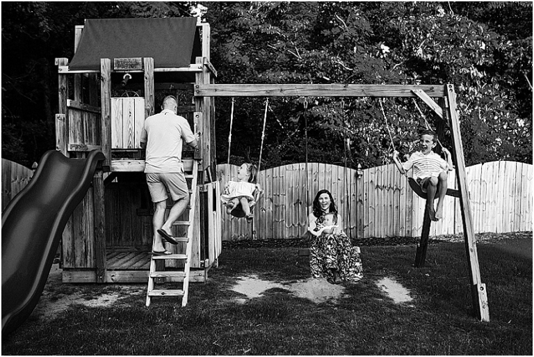 Black and white portrait of a family of 5 on their backyard swingset.
