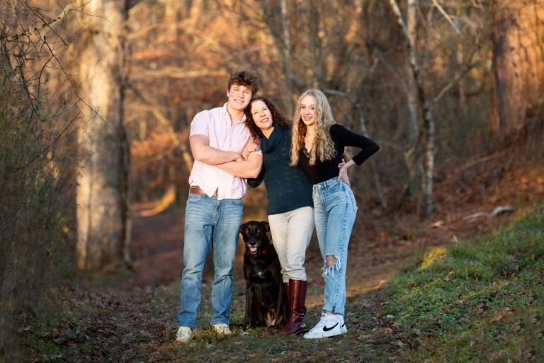 mom hugging her two older kids, with their black german shepard sitting alongside them.